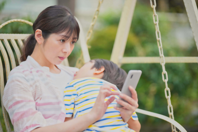 子どもを抱きながらスマホ操作をする母親